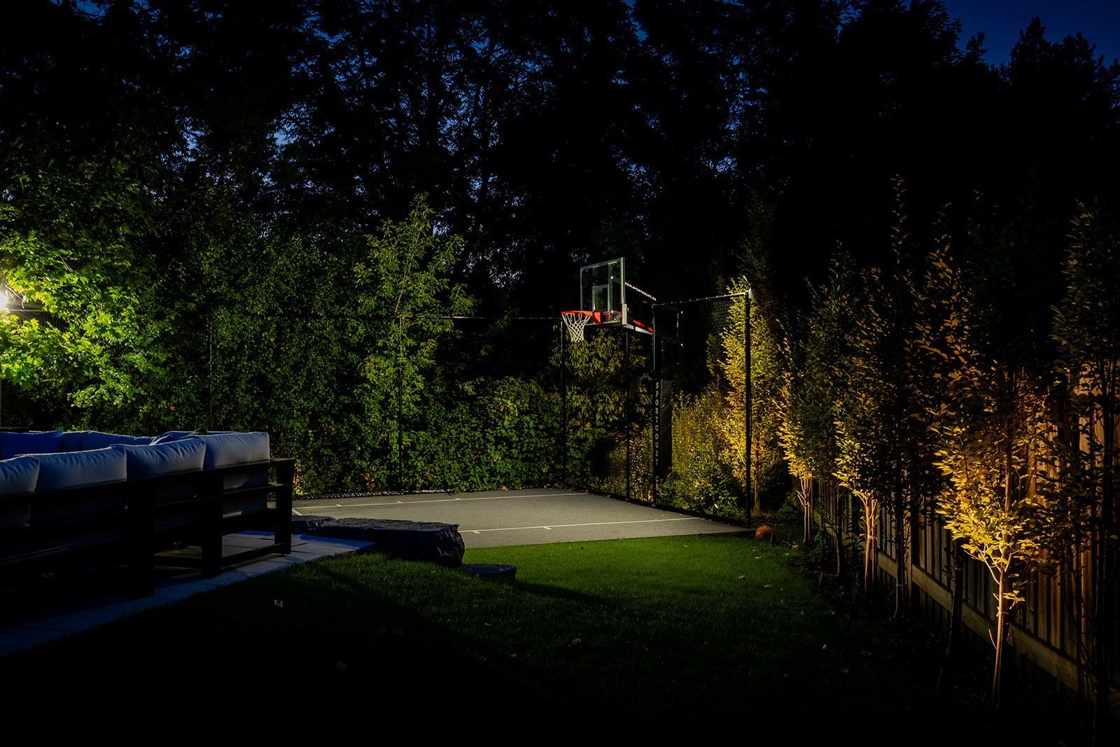 A practice basketball court lit up in the dark outside in the backyard.