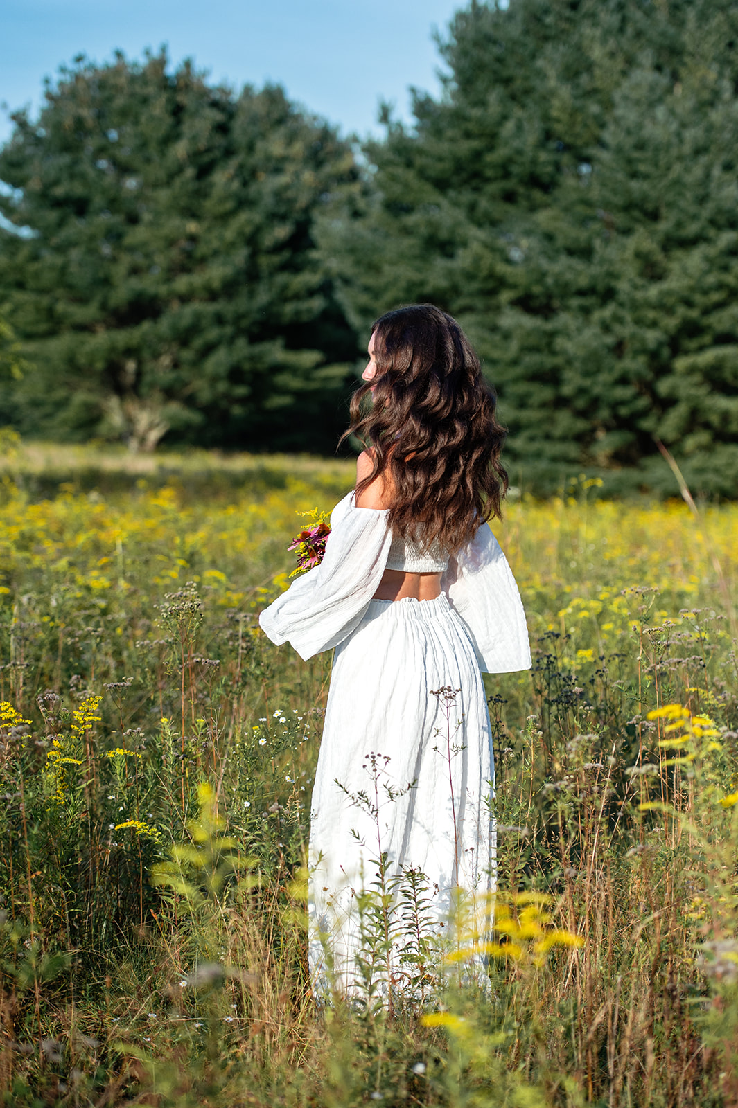 Brown-haired high school senior girl twirling in a field of wildflowers while her dress and hair flow through the air. 