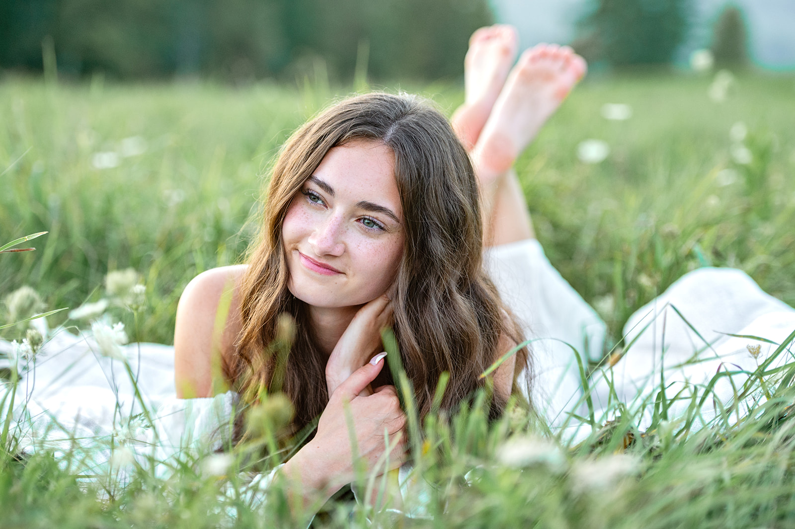 A high school senior lays in a field of green grass and queen anne's lace on stomach with feet crossed. 