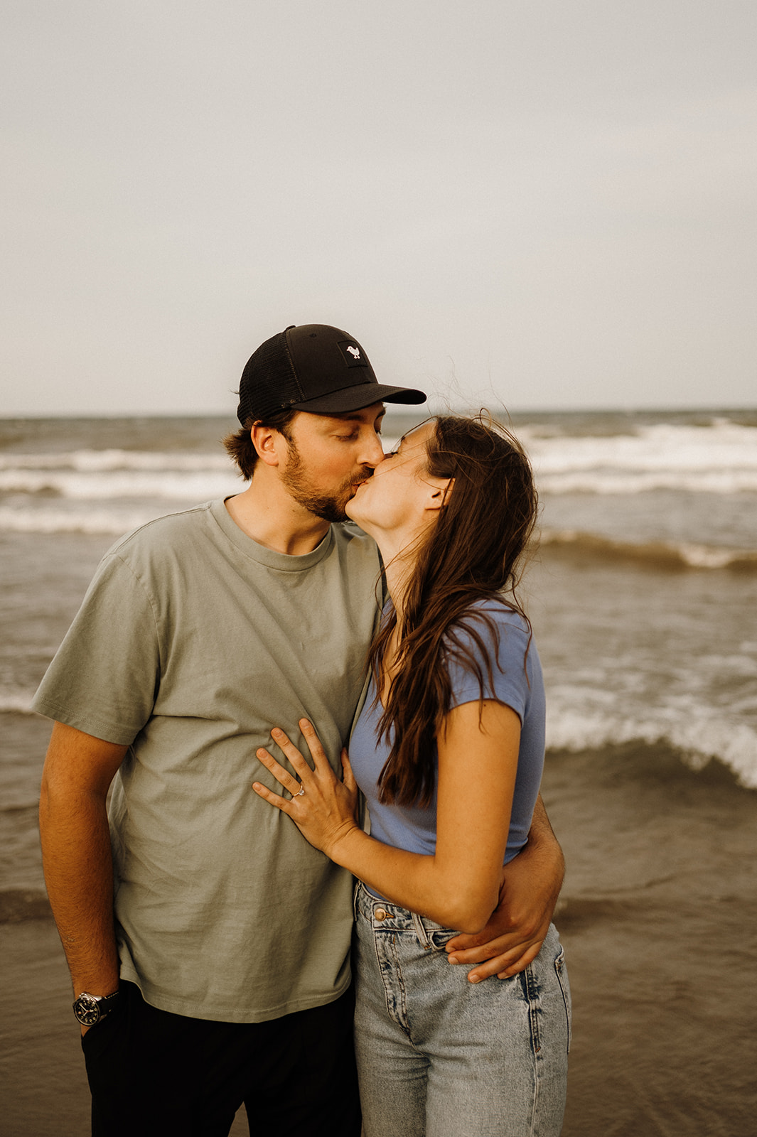 A man and woman kissing standing on the beach.