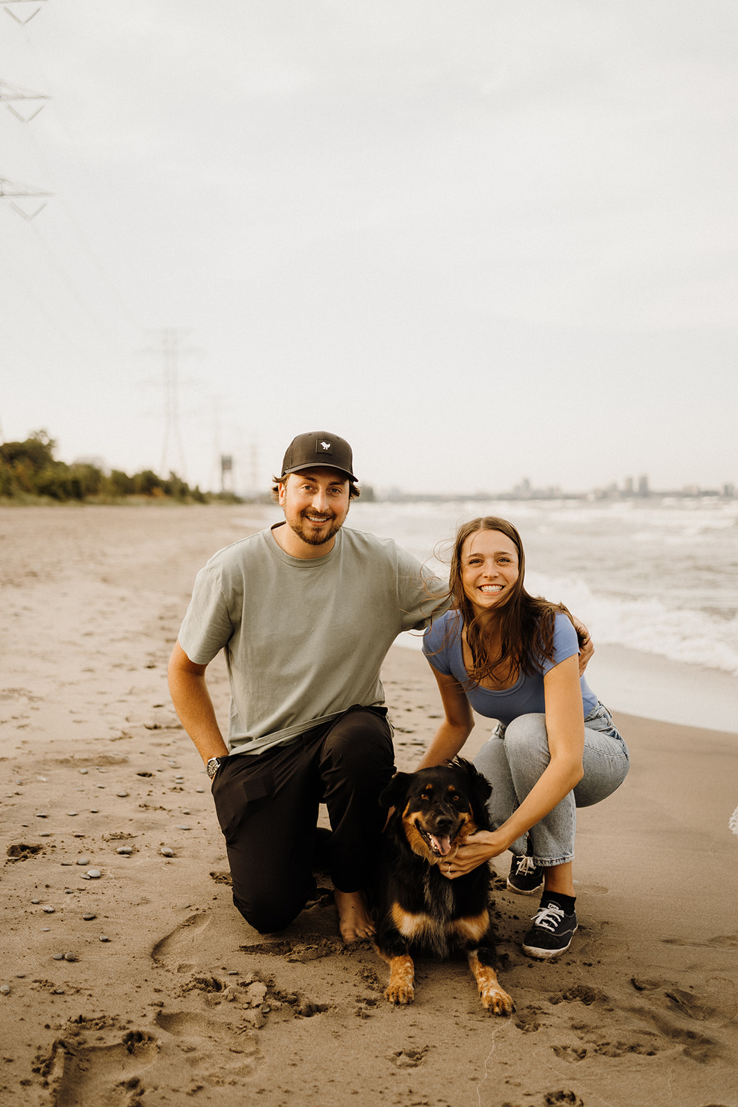 A man and woman sitting on the beach with their dog.