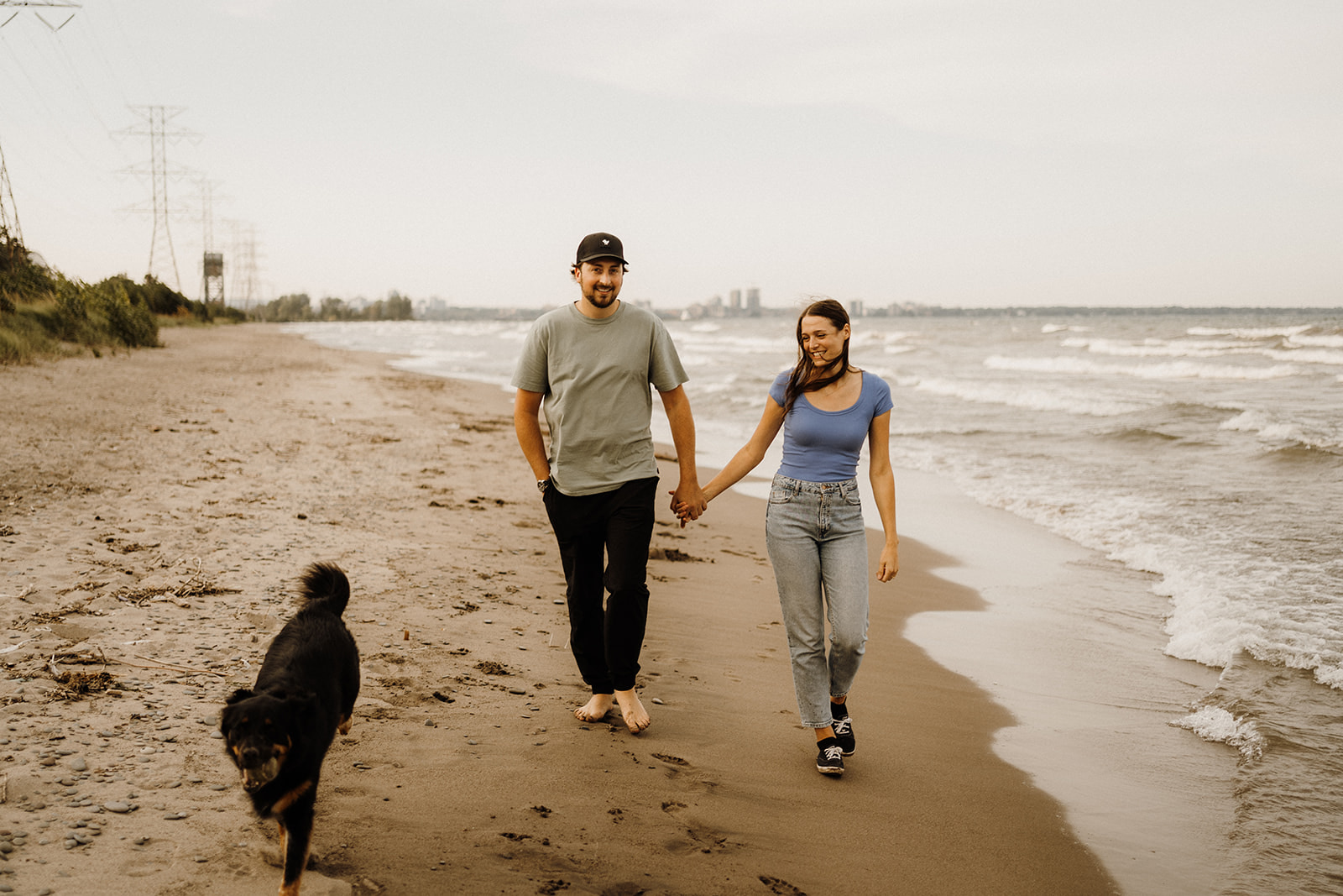A man and woman walking down the beach with their dog.
