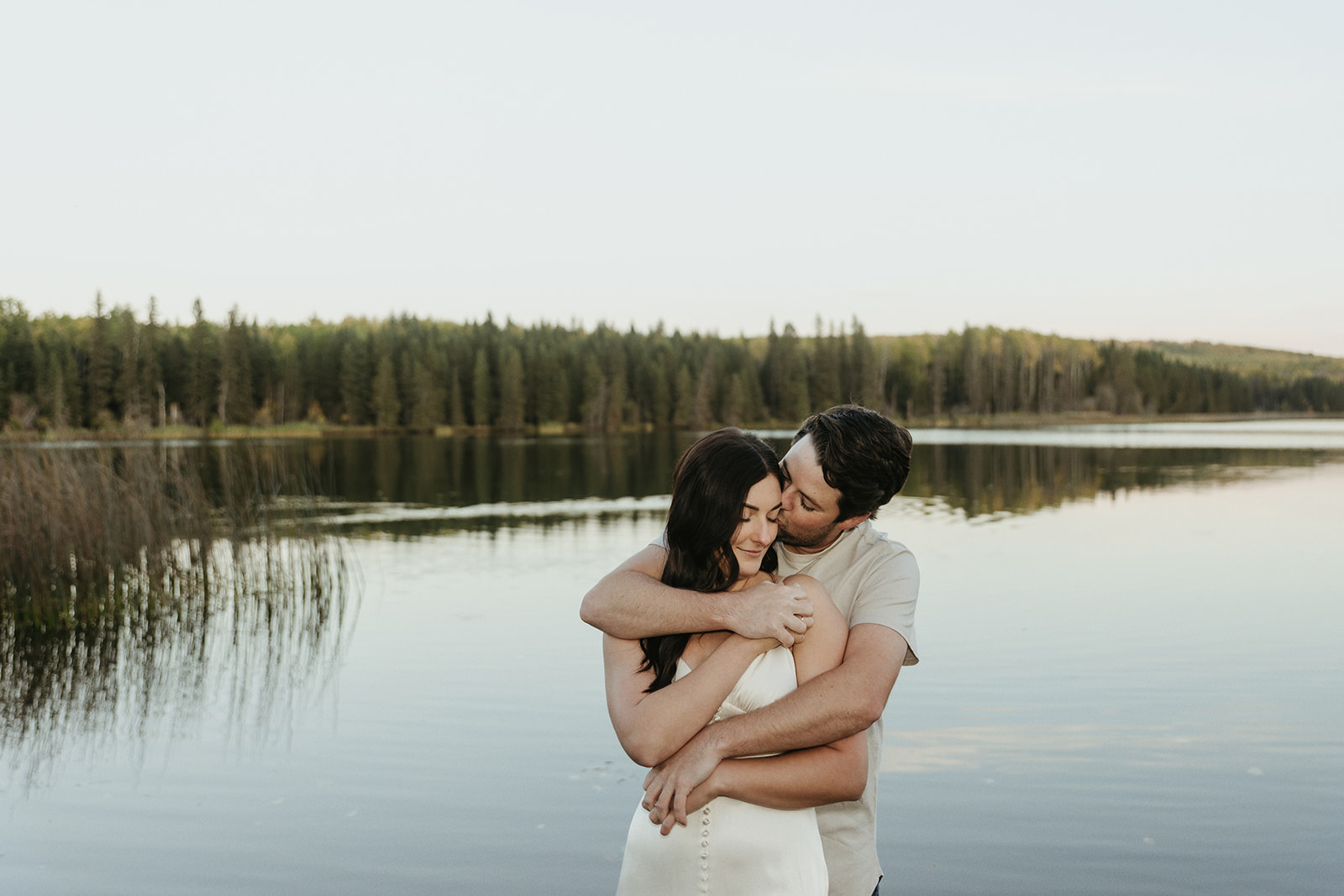 couple embraces each other on the edge of the lake during blue hour for their engagement photos