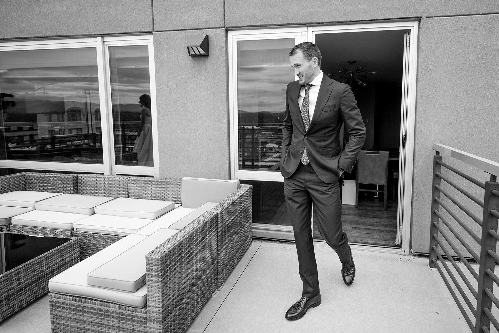 black and white photo of groom walking to bride for first look with the bride in the reflection of the glass