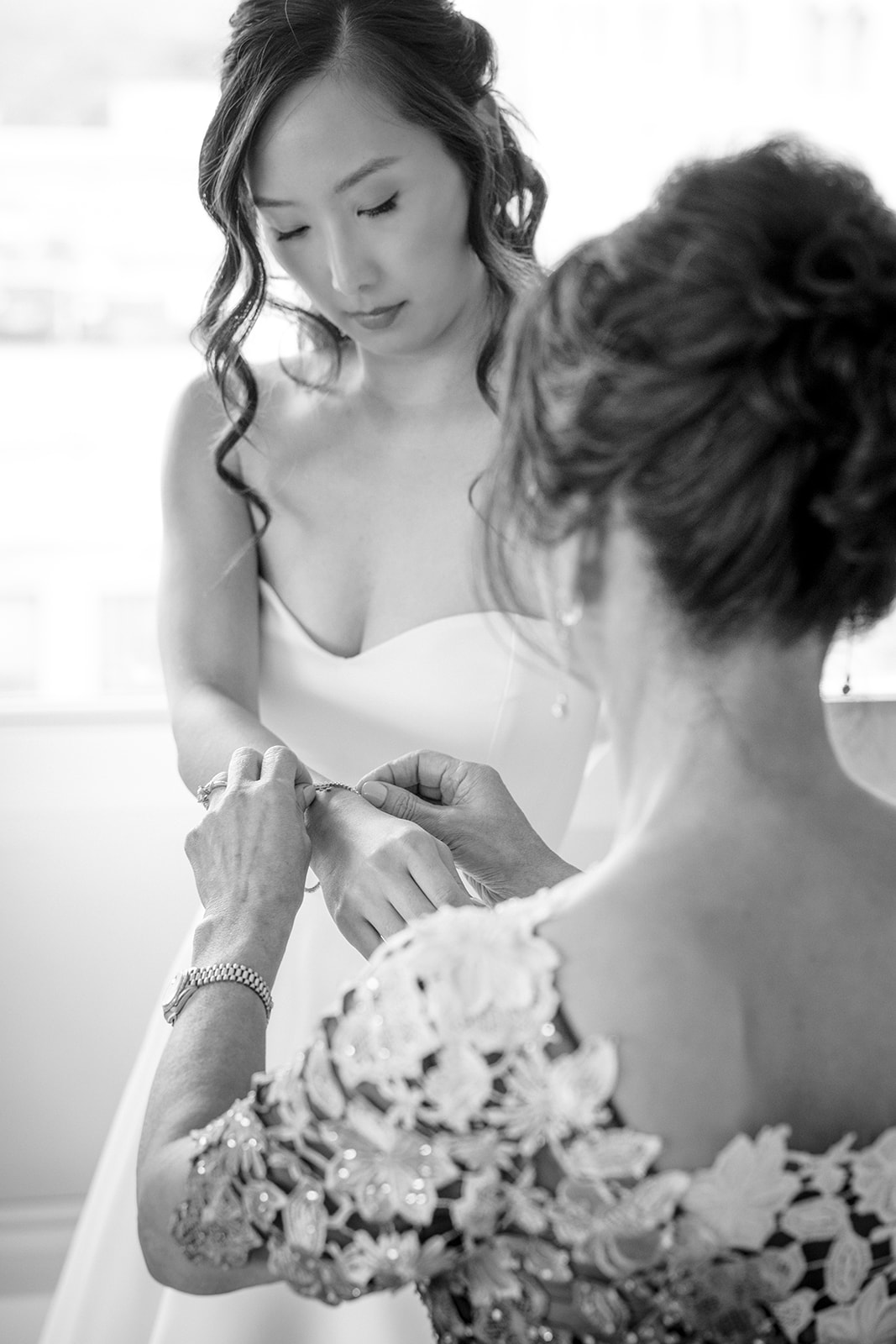 black and white photo of the mother of the bride helping bride put on diamond tennis bracelet 
