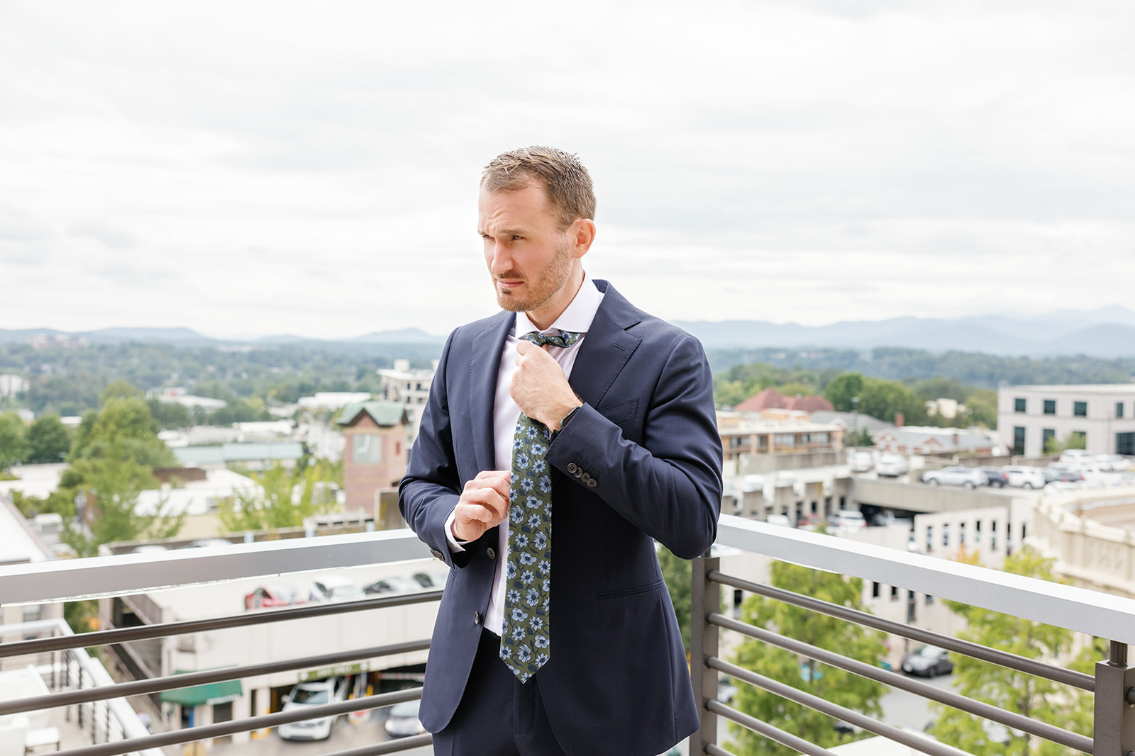 groom adjusts his tie with Asheville mountains in the background 
