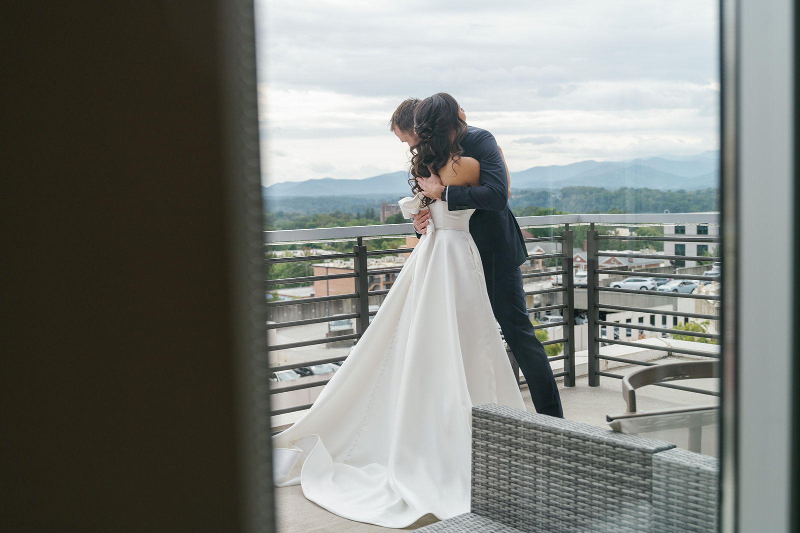 Looking through the window at bride and groom sharing a first look with Asheville city scape in the background.  Photogr
