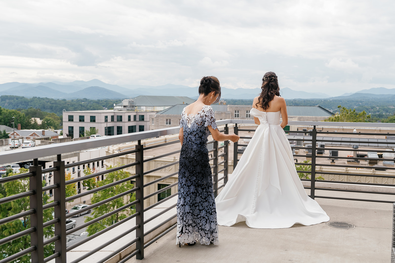 Mother of the bride straightens brideds dress on private balcony overlooking downtown asheville