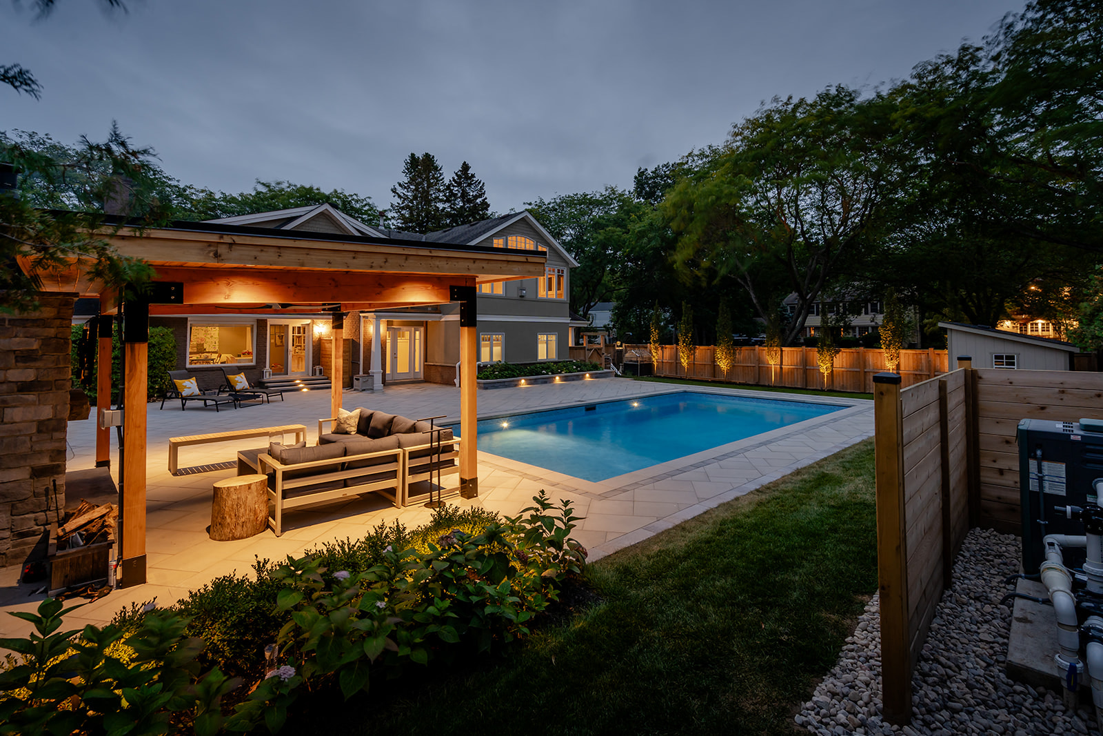 A backyard with an inground pool and lights on in the gazebo.