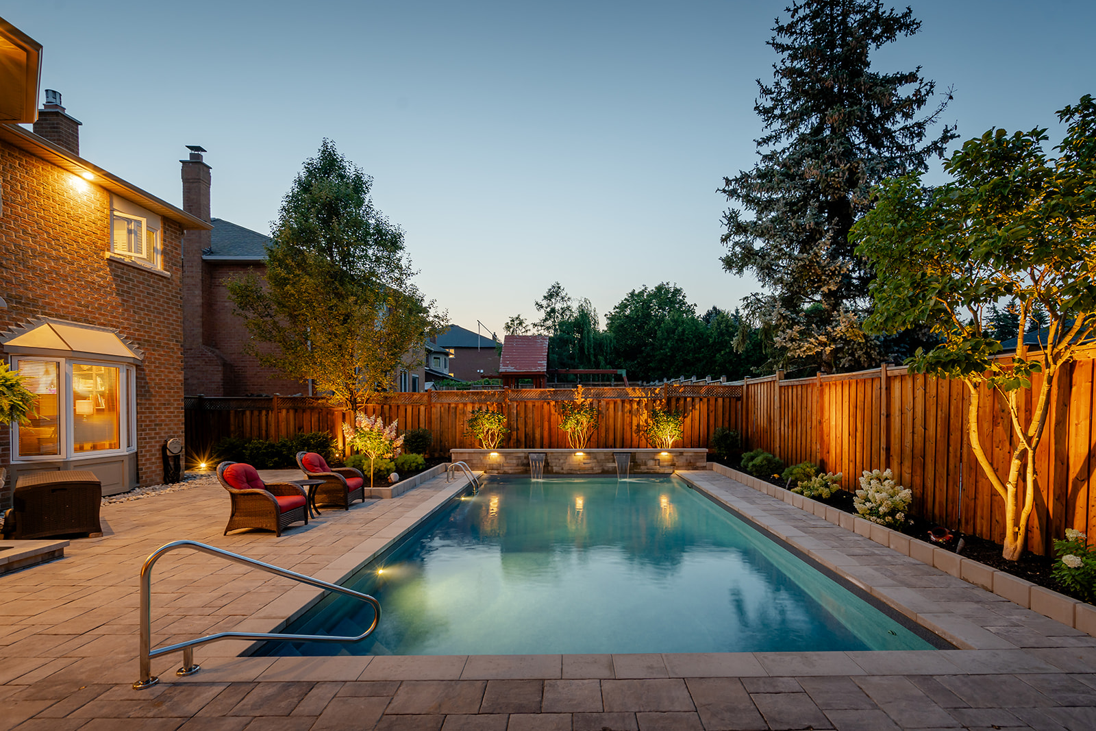 An inground pool with patio chairs on the left and two mini waterfalls flowing int the pool in the back.