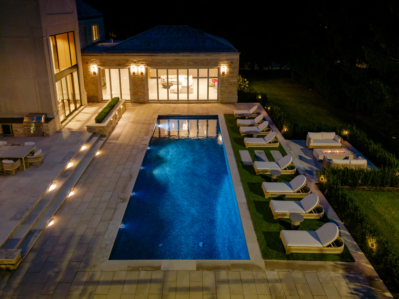 A done-shot of the backyard with the inground pool and the house lit up.