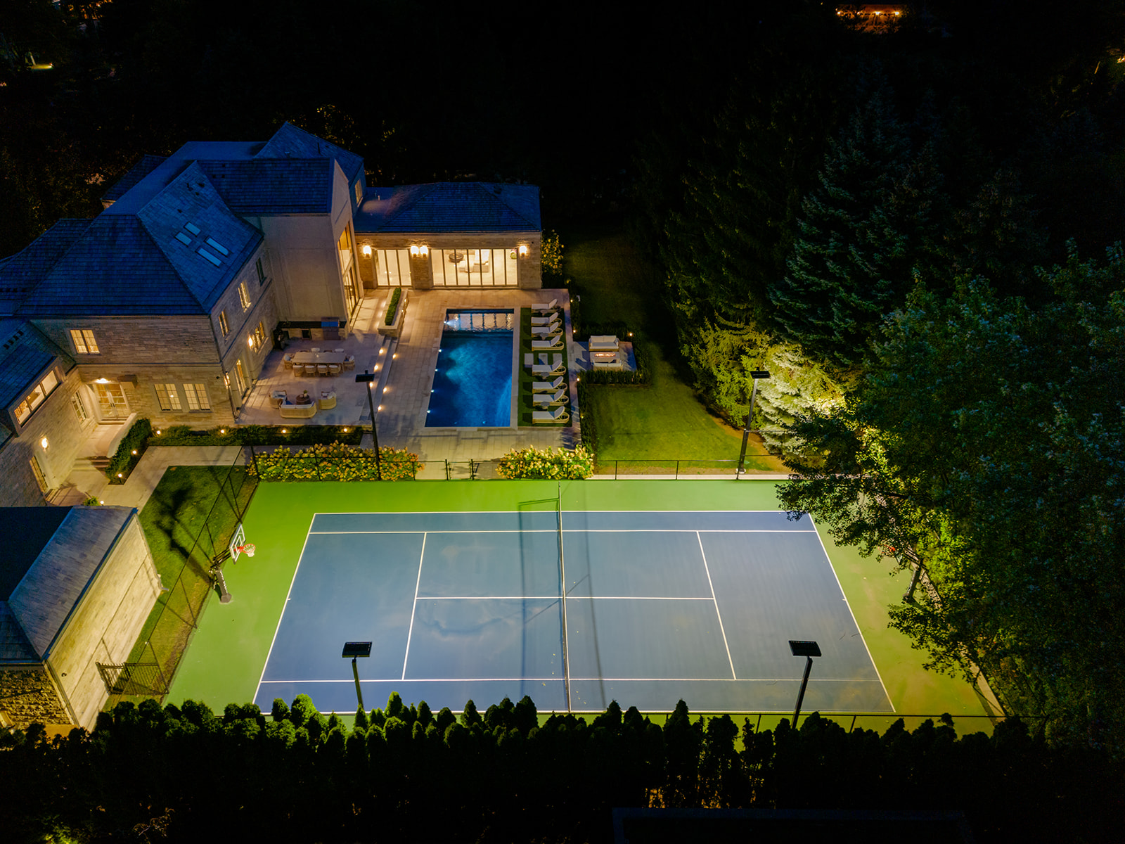 A done-shot of the backyard with the  tennis court lit up.