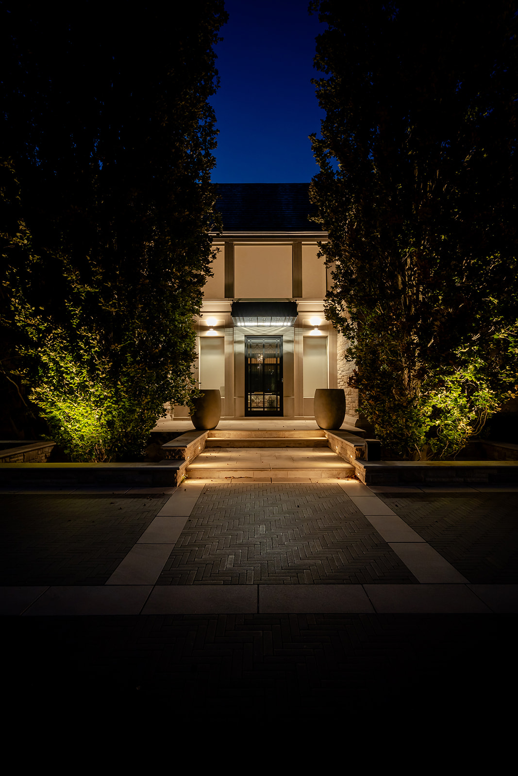 A large driveway leading to the house with lights on.