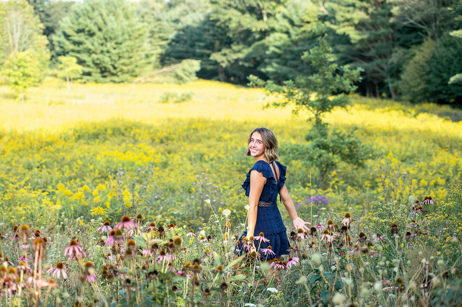 A beautiful senior girl walking softly through a wildflower field looking over her shoulder. 