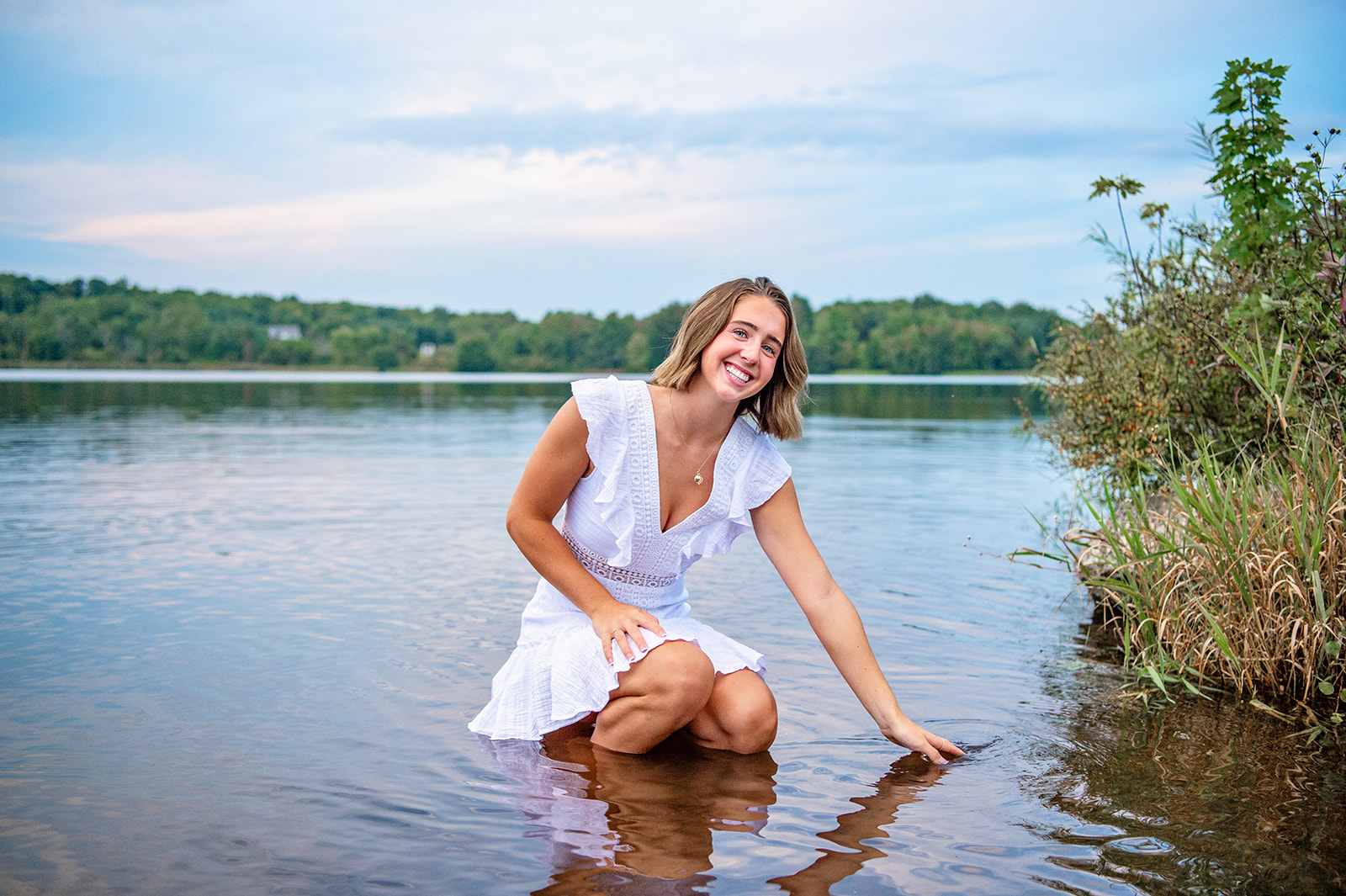 Senior girl squatting down in a lake softly touching the water and smiling. 