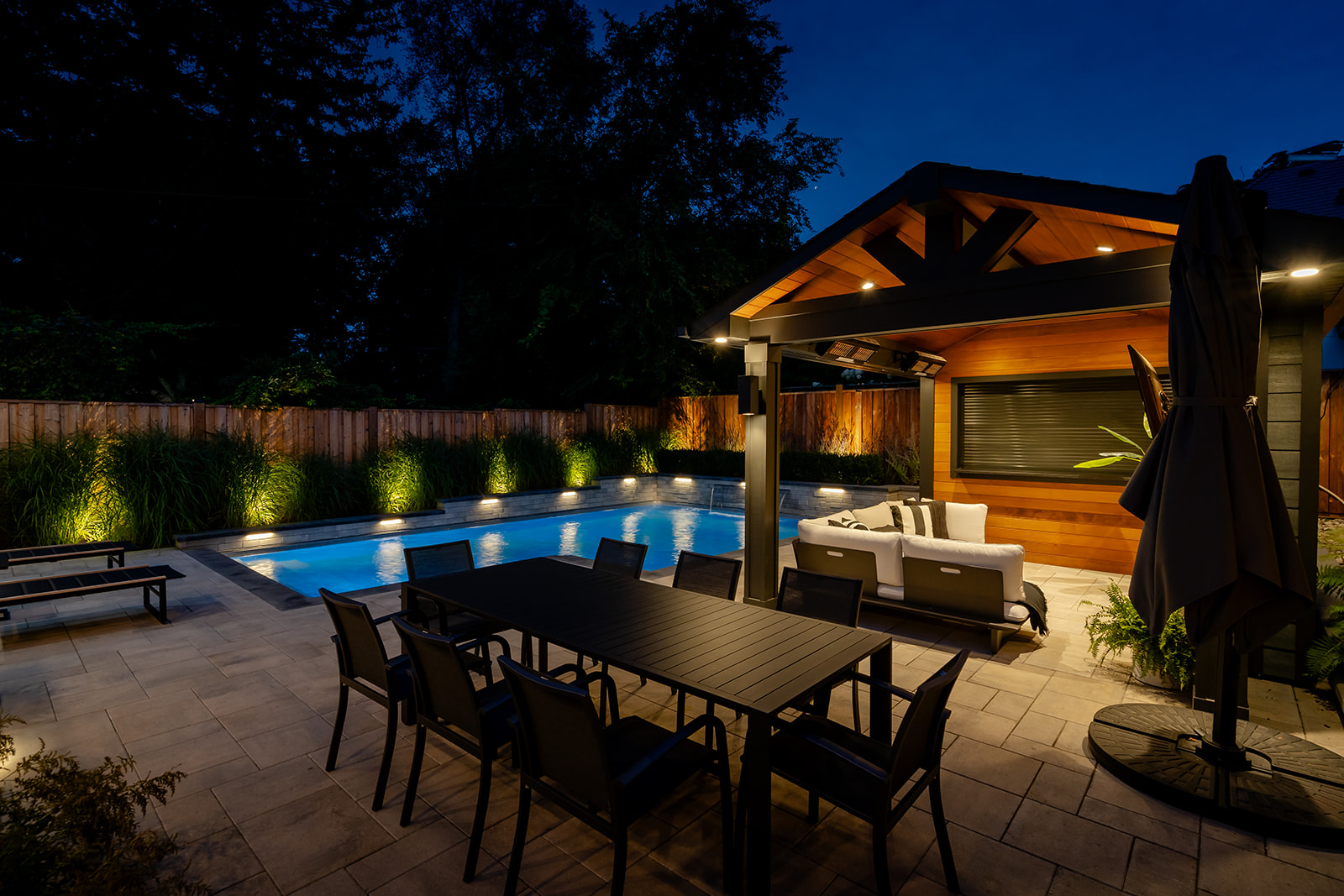 An outdoor patio set with the pool in the background with lights on.