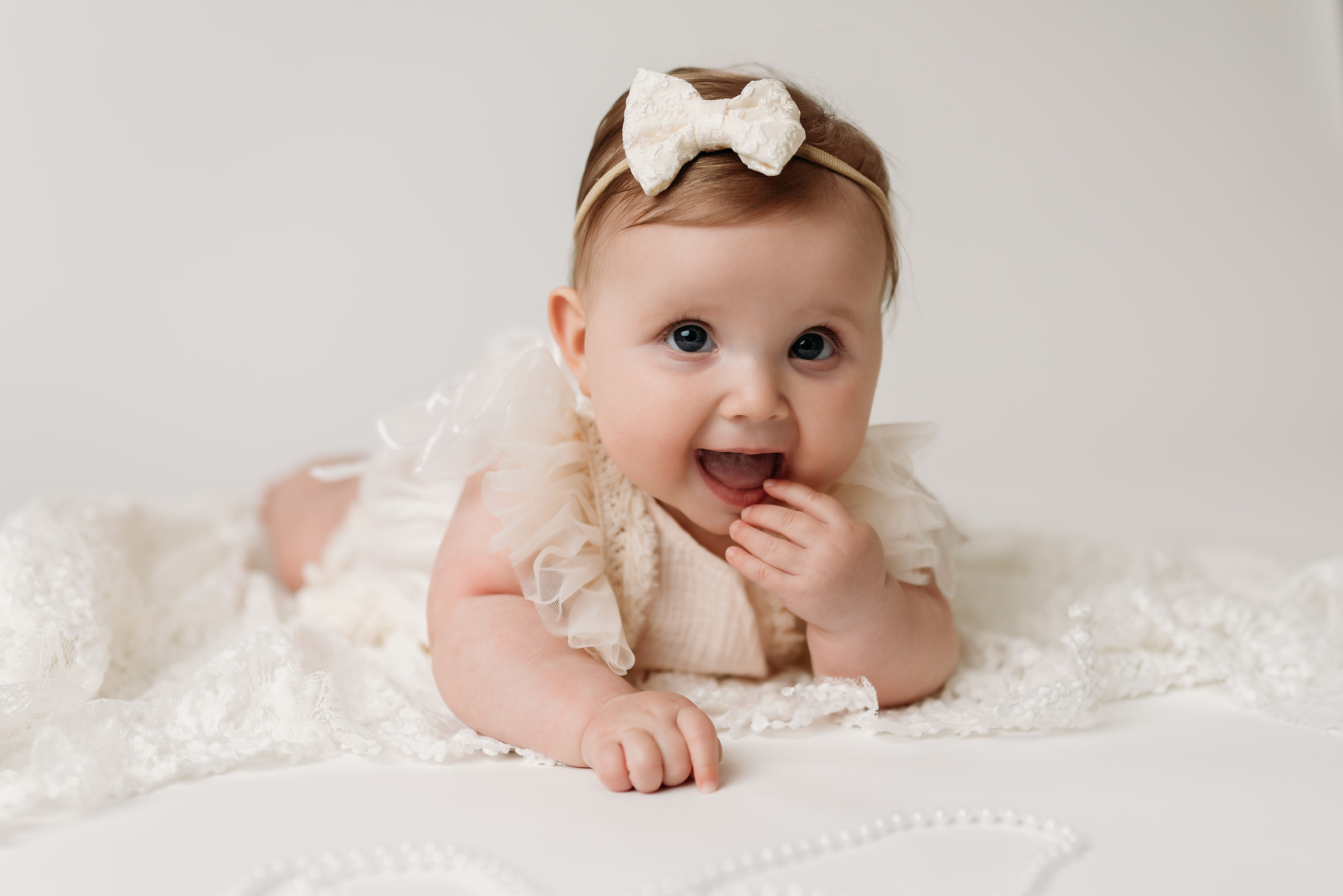 Cute 6 month old showing off tummy time on a white backdrop during her 6 month milestone photo shoot