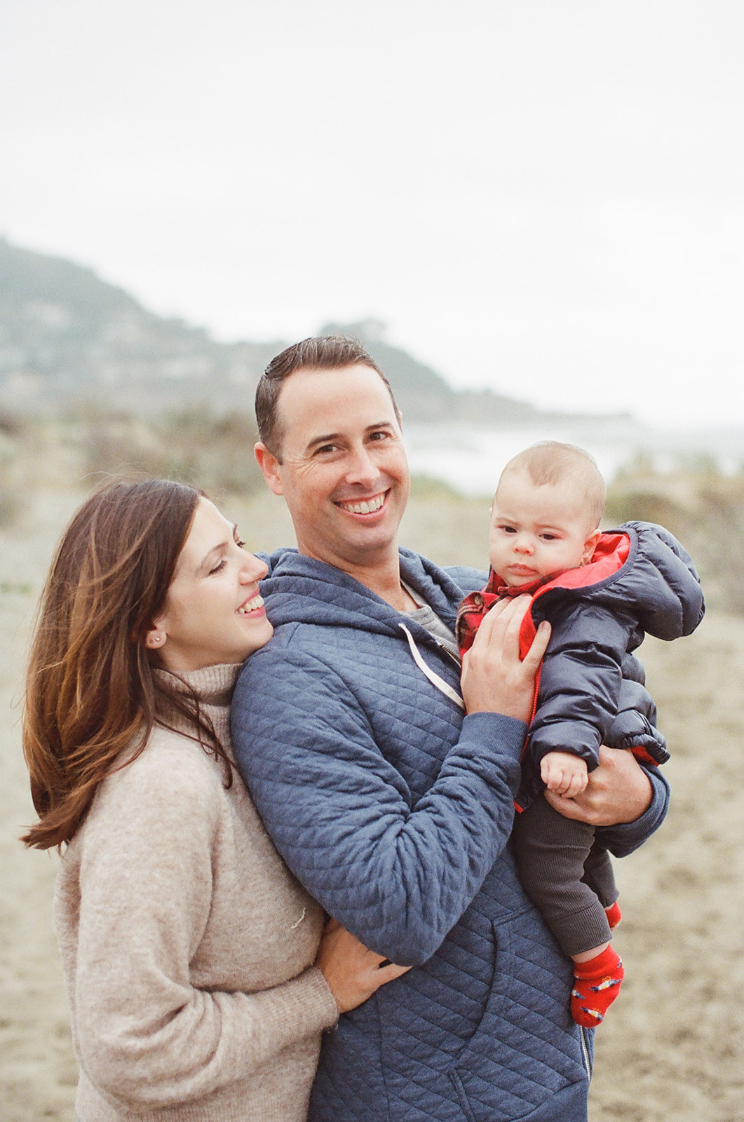 A young family snuggles their baby boy on a beach in Pacifica