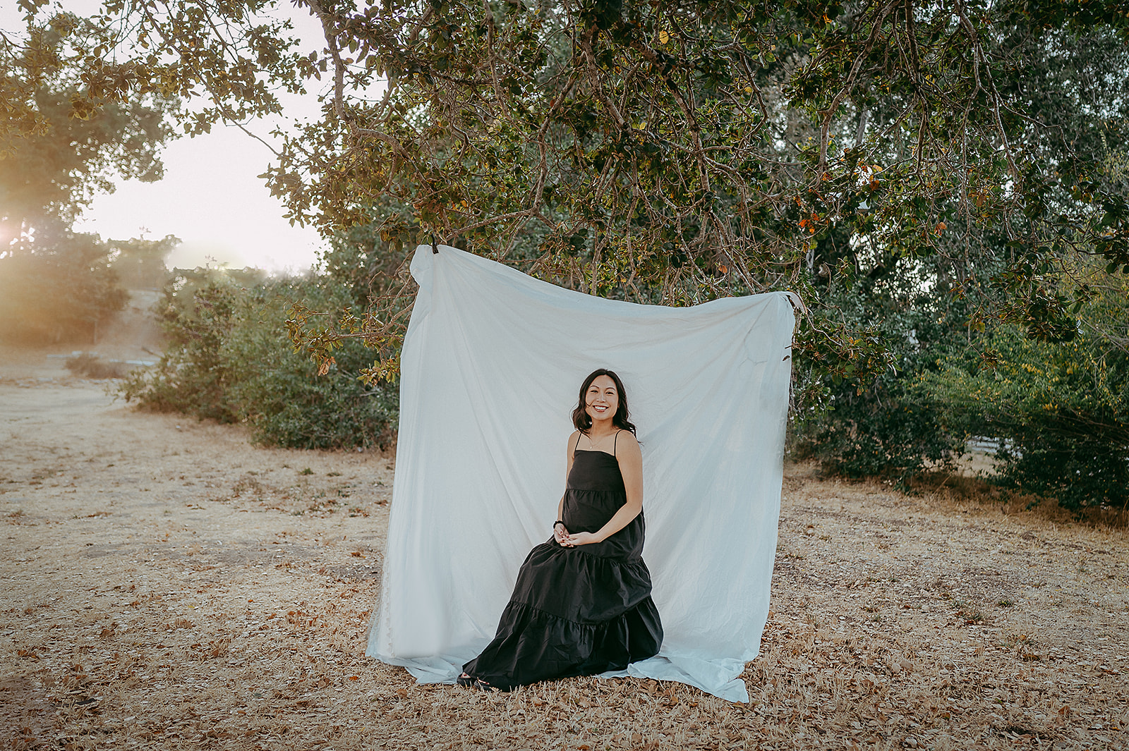 Maternity photos in front of a white cloth hanging from a tree