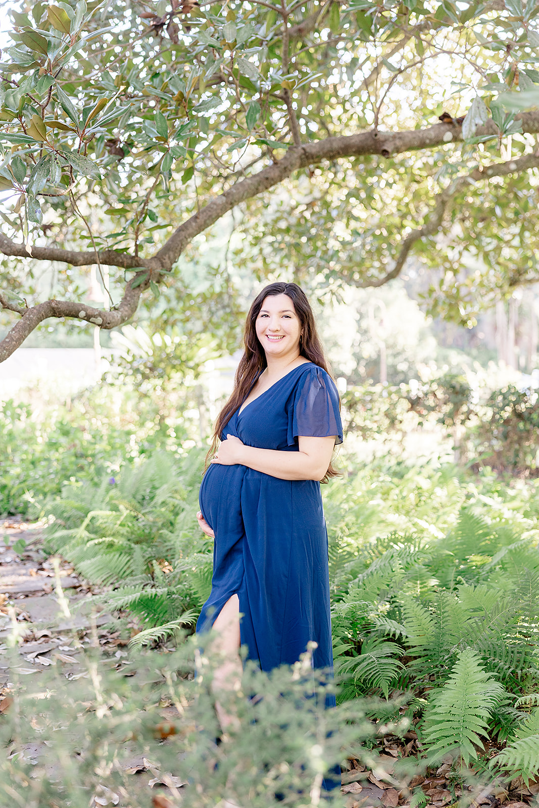 pregnant mom in navy dress long dark hair outdoors under arch of a green tree