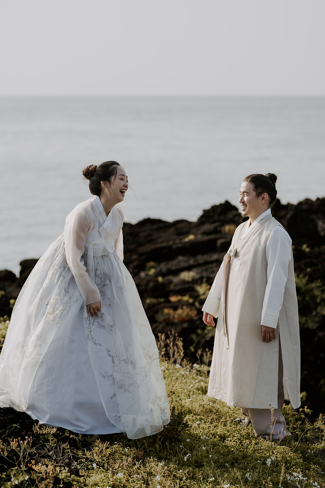 Asian couple in traditional hanbok standing next to the ocean during their pre-wedding photoshoot in Korea.