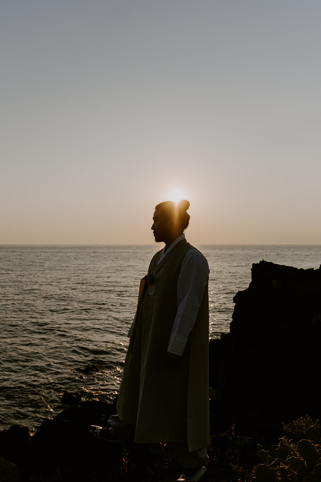 A man standing on a cliff in Korea overlooking the ocean during a pre-wedding photoshoot.