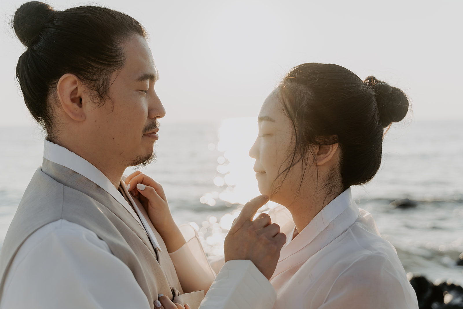 A man and woman in traditional Korean clothing standing by the ocean in Korea for their pre-wedding shoot.