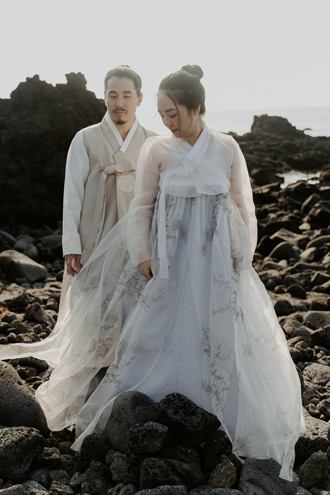 A pre-wedding couple standing on rocks near the ocean.