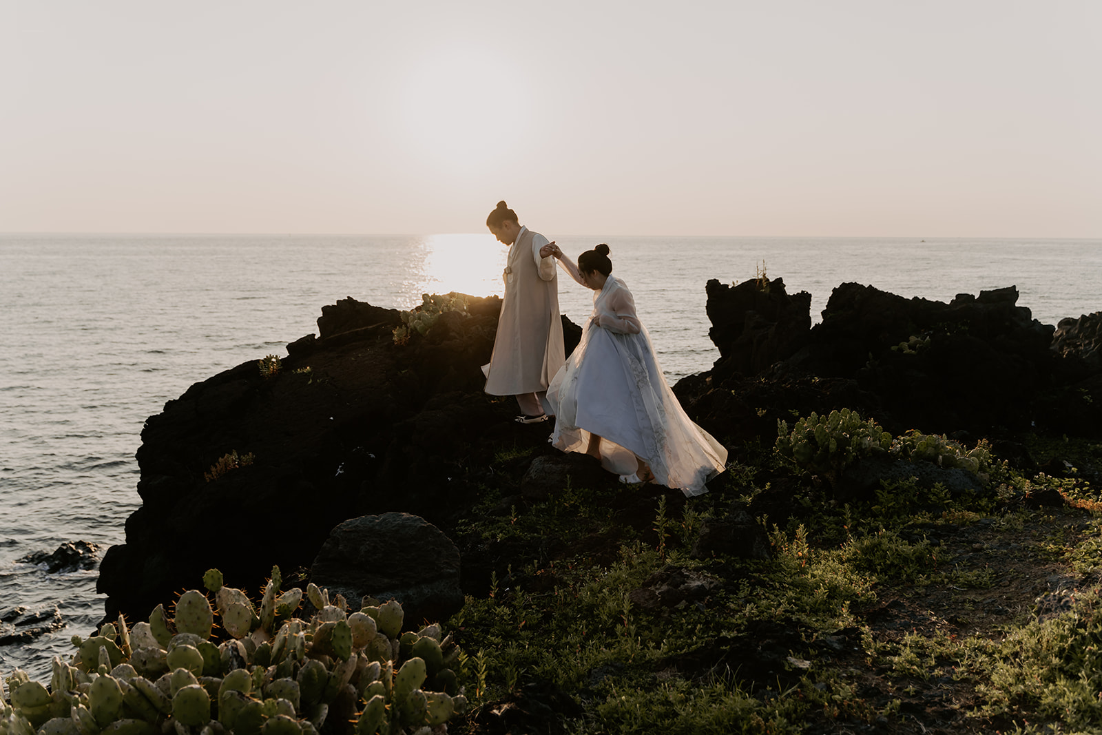 A pre-wedding couple standing on a rocky cliff overlooking the ocean in Korea.