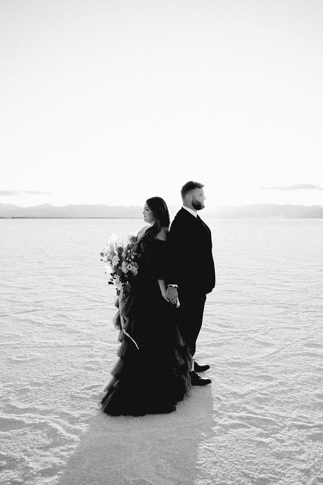 Black and white photo of a couple at the Salt Flats, looking into the distance, with a large floral bouquet
