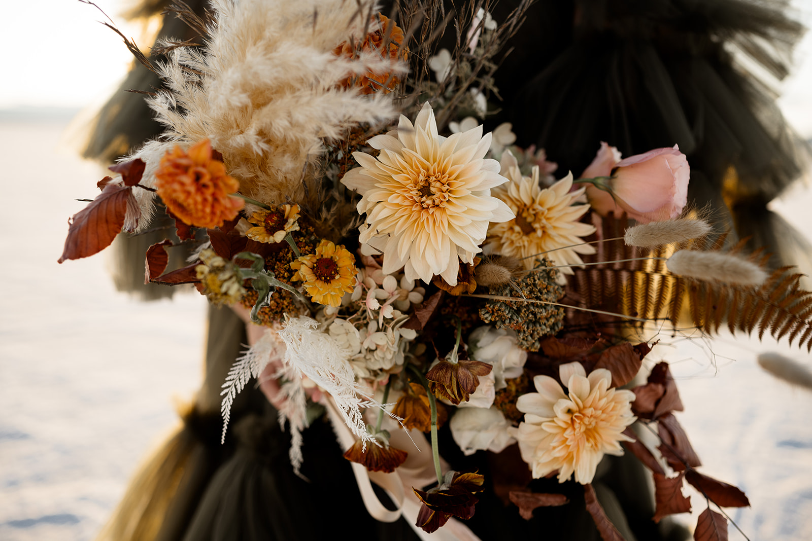 Close-up of a detailed floral bouquet with white, peach, and dark flowers, set against a dark background