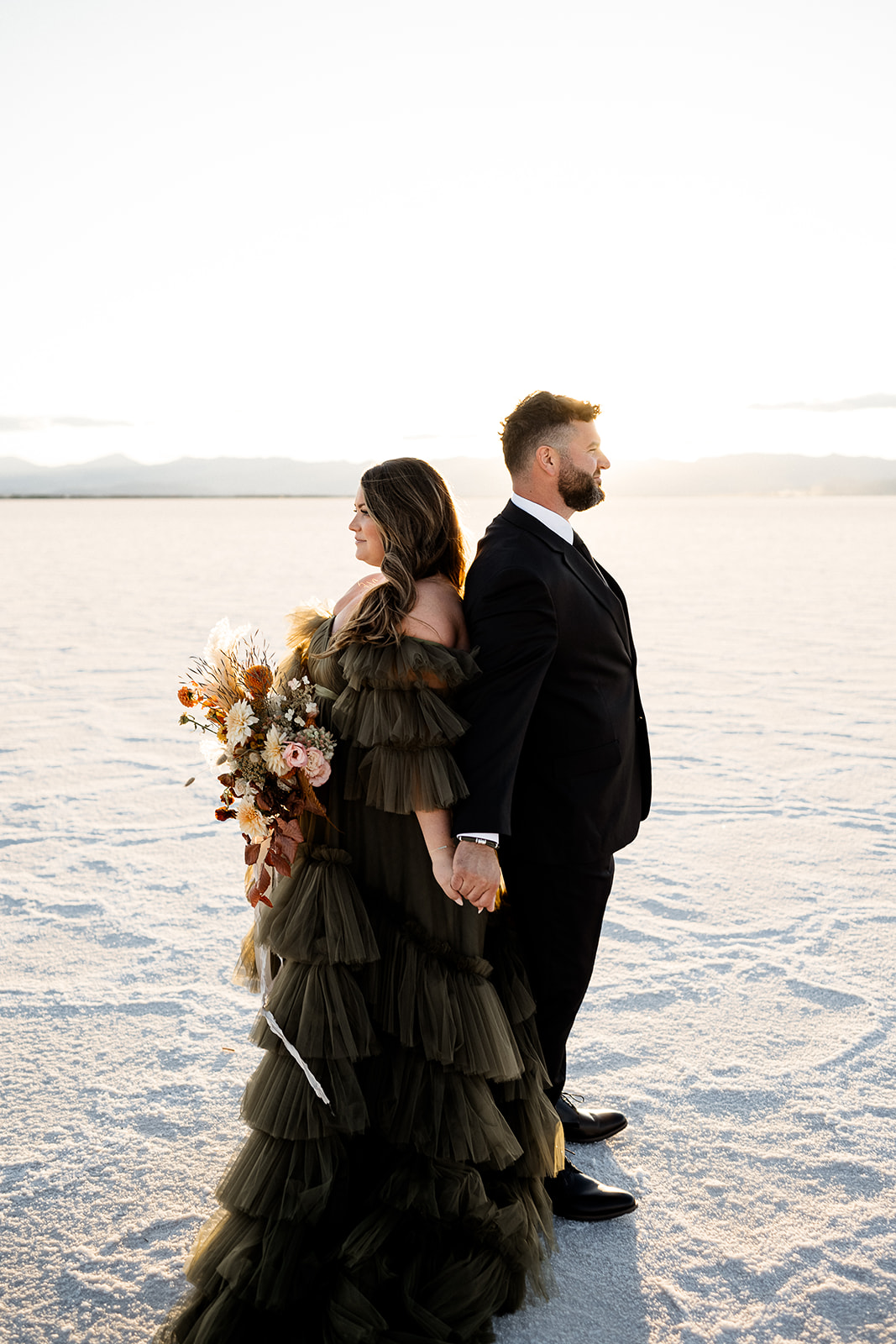 Couple at the Salt Flats, leaning back to back in formal attire with the white textured salt