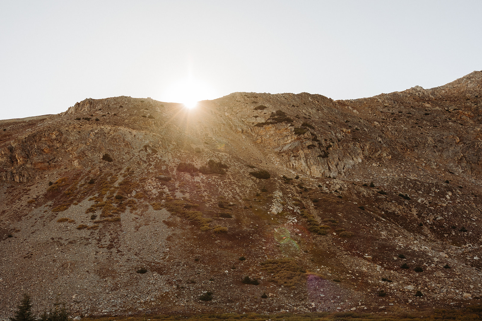 The sun peaking out from a tall hill in the mountains as it sets for this rocky Colorado engagement session.