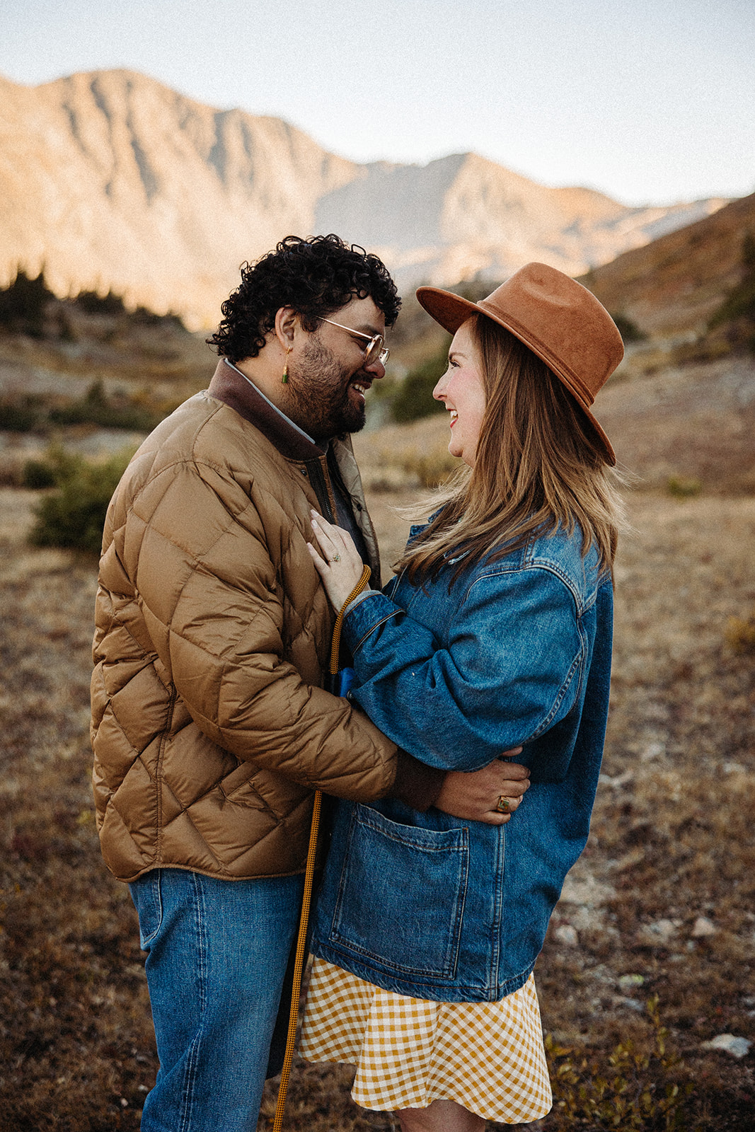 The fiances smile and look deeply into each other's eyes while the tall mountains ignite with the golden hour light.