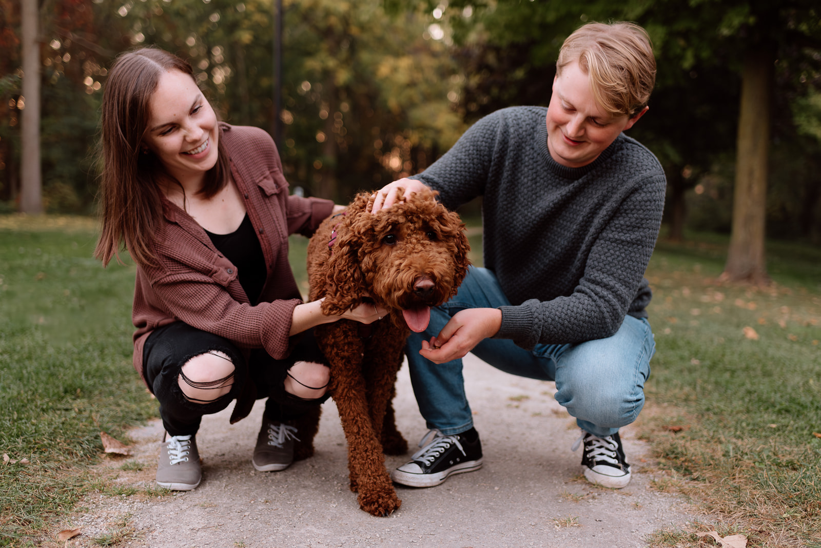 An engaged couple and their dog taking a walk through the autumn leaves during an engagement session. 