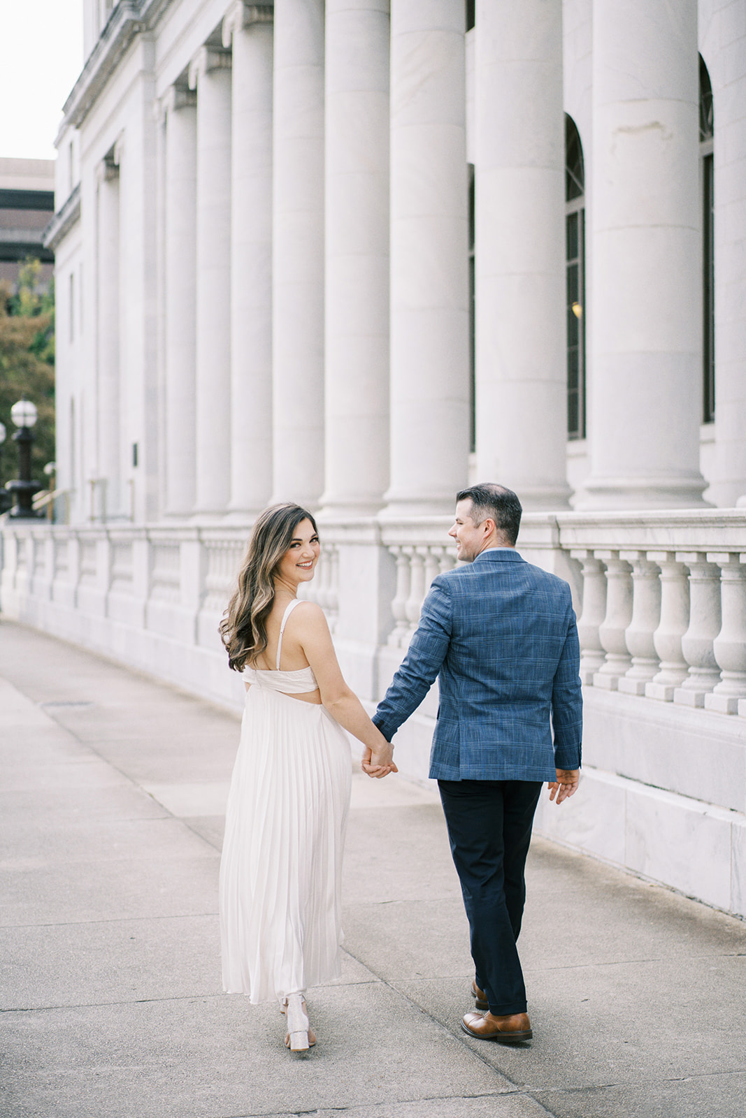 A couple walks down the street during a romantic engagement session in front of the Robert S. Vance Federal Building