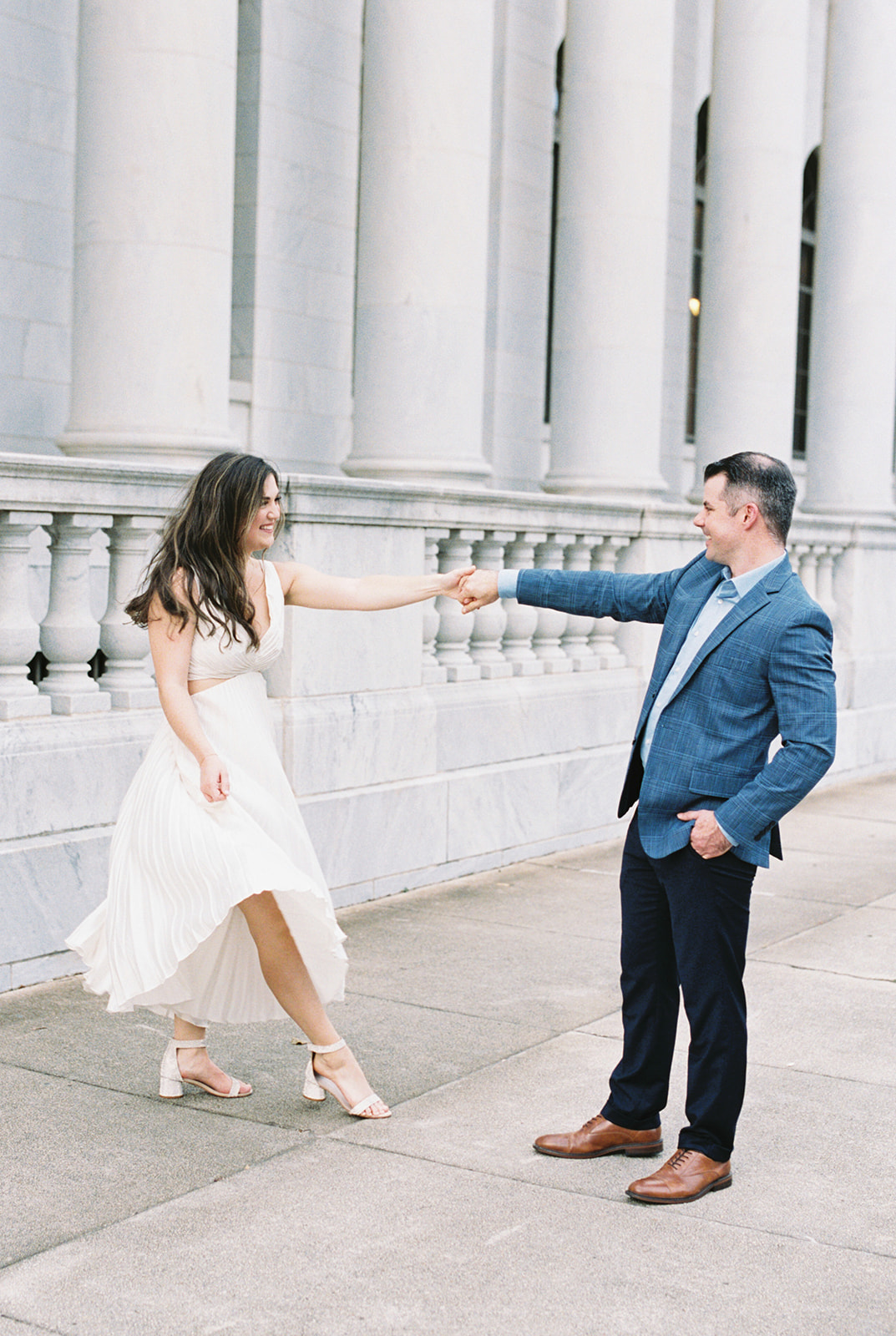 A couple dances on the sidewalk during a romantic engagement session in front of the Robert S. Vance Federal Building