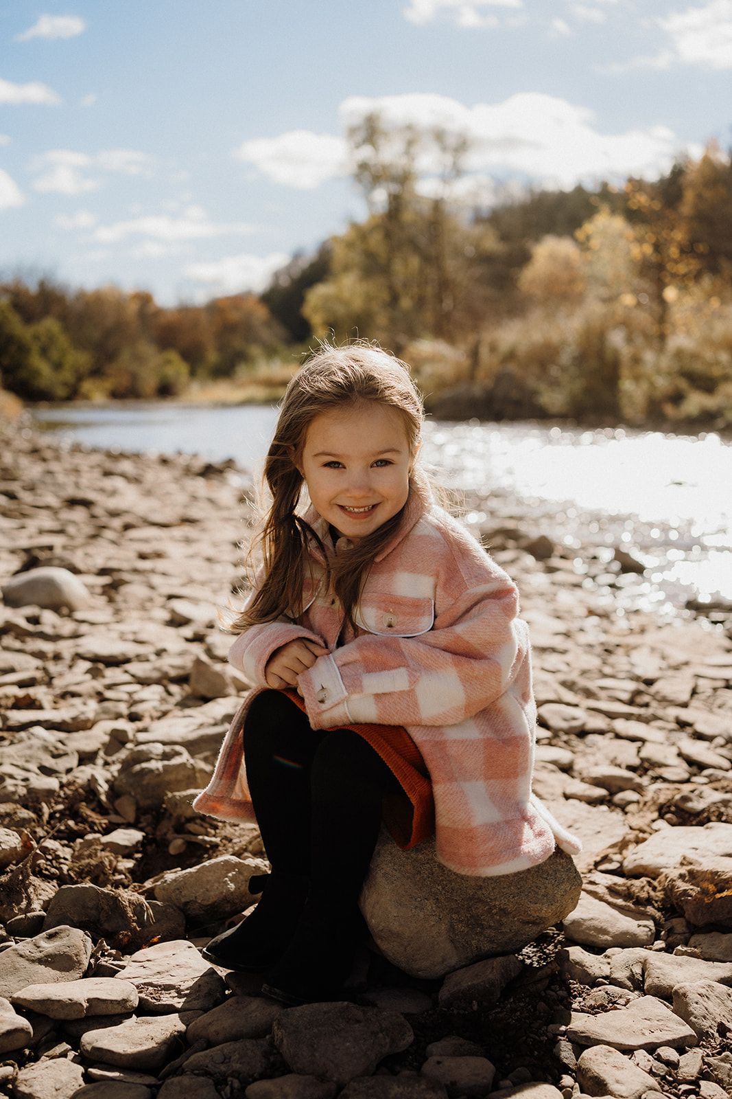 A little girl sitting on a rock outside.