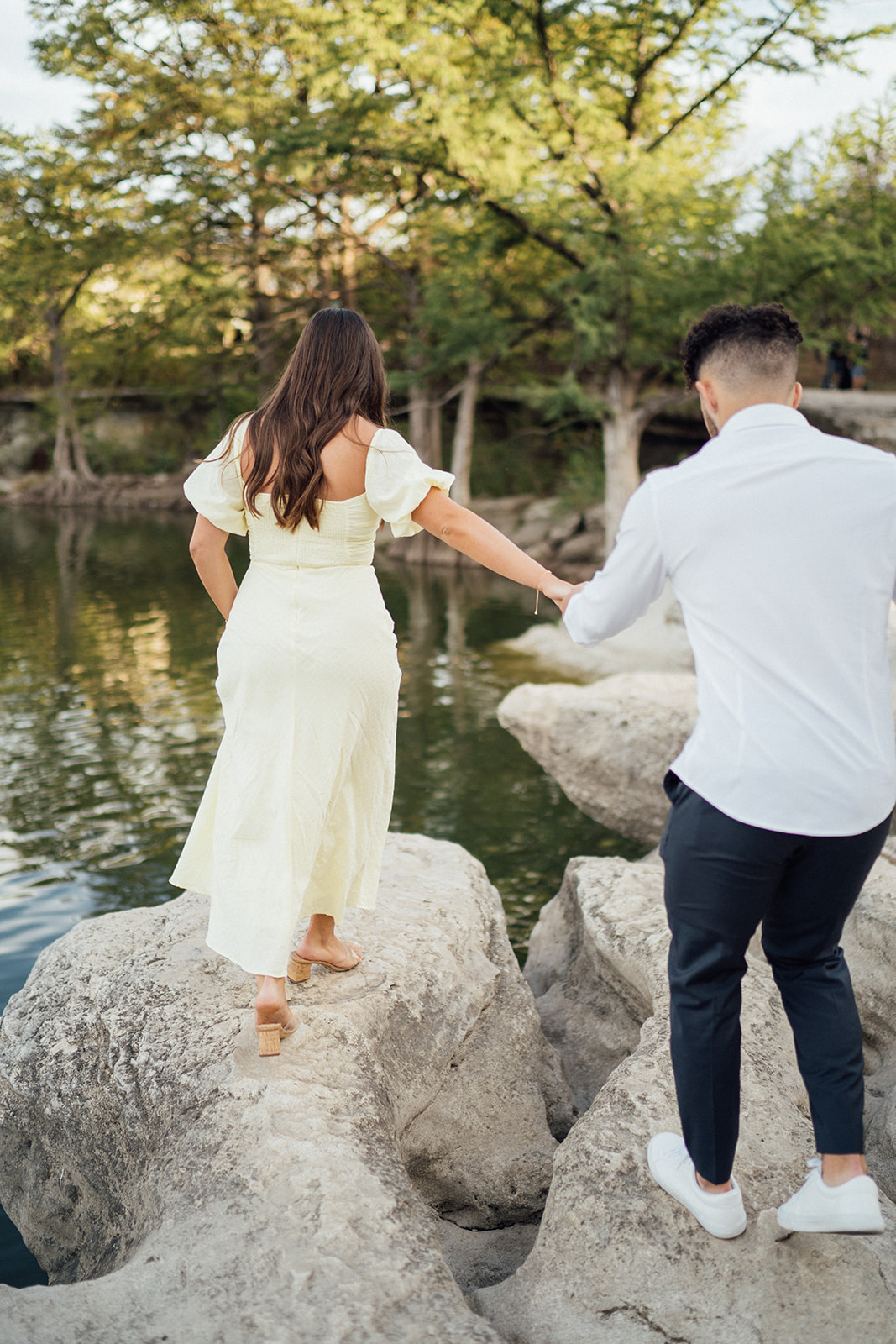 A couple embraces during engagement photography session on a boulder overlooking McKinney Falls.