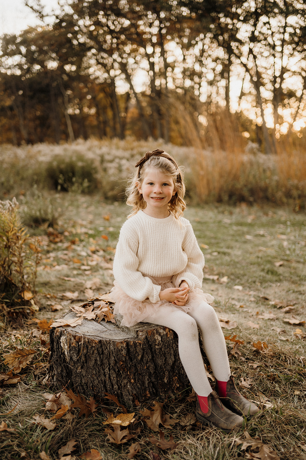 A little girl sitting on a rock outside.