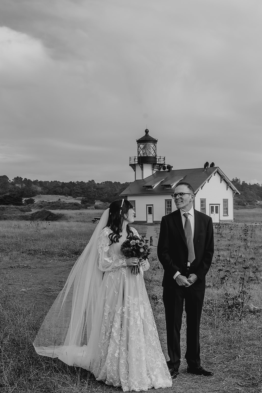 a black and white photo of a bride walking down the aisle with the point cabrillo lighthouse as their backdrop