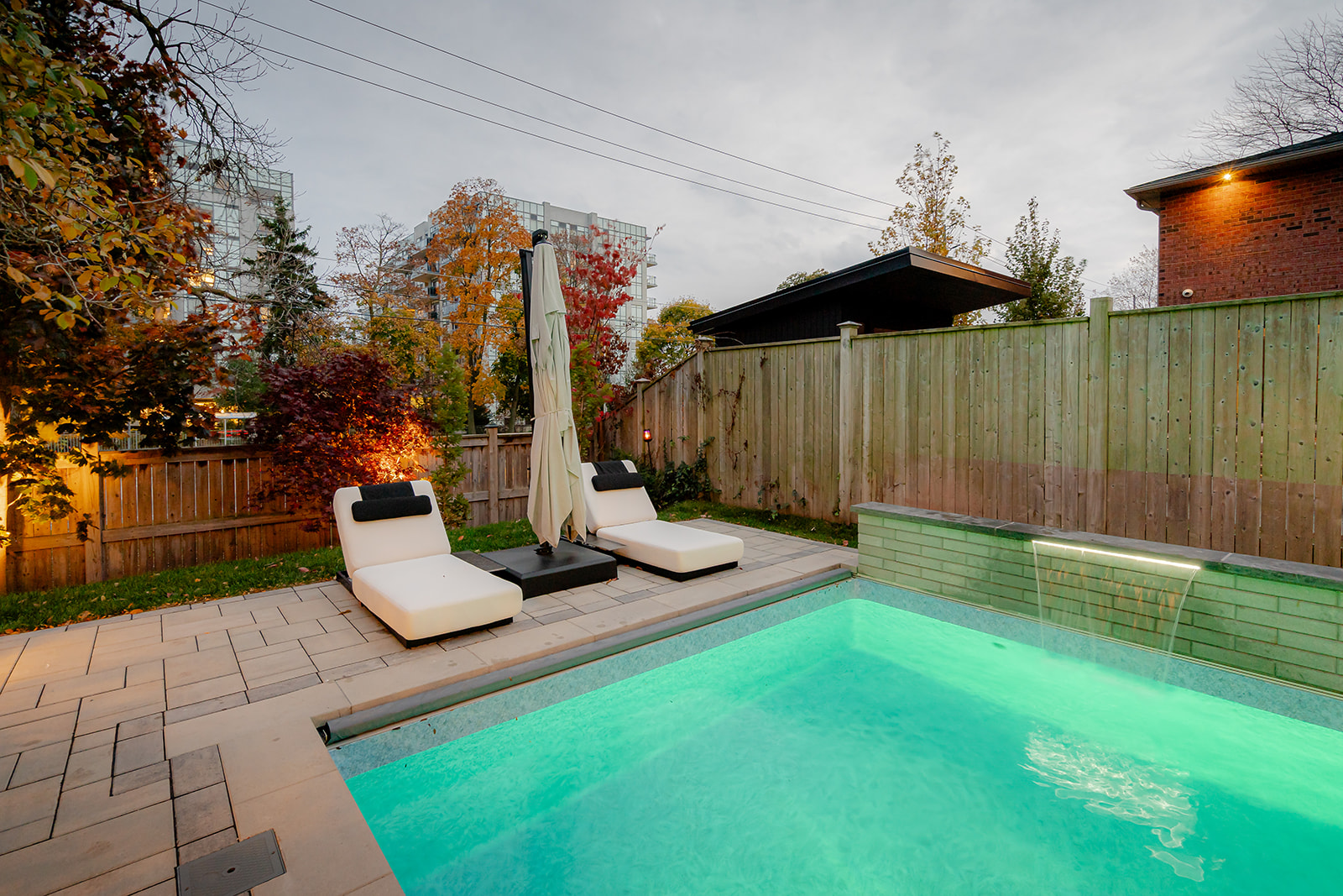 An inground pool with the waterfall on and chairs on the patio.