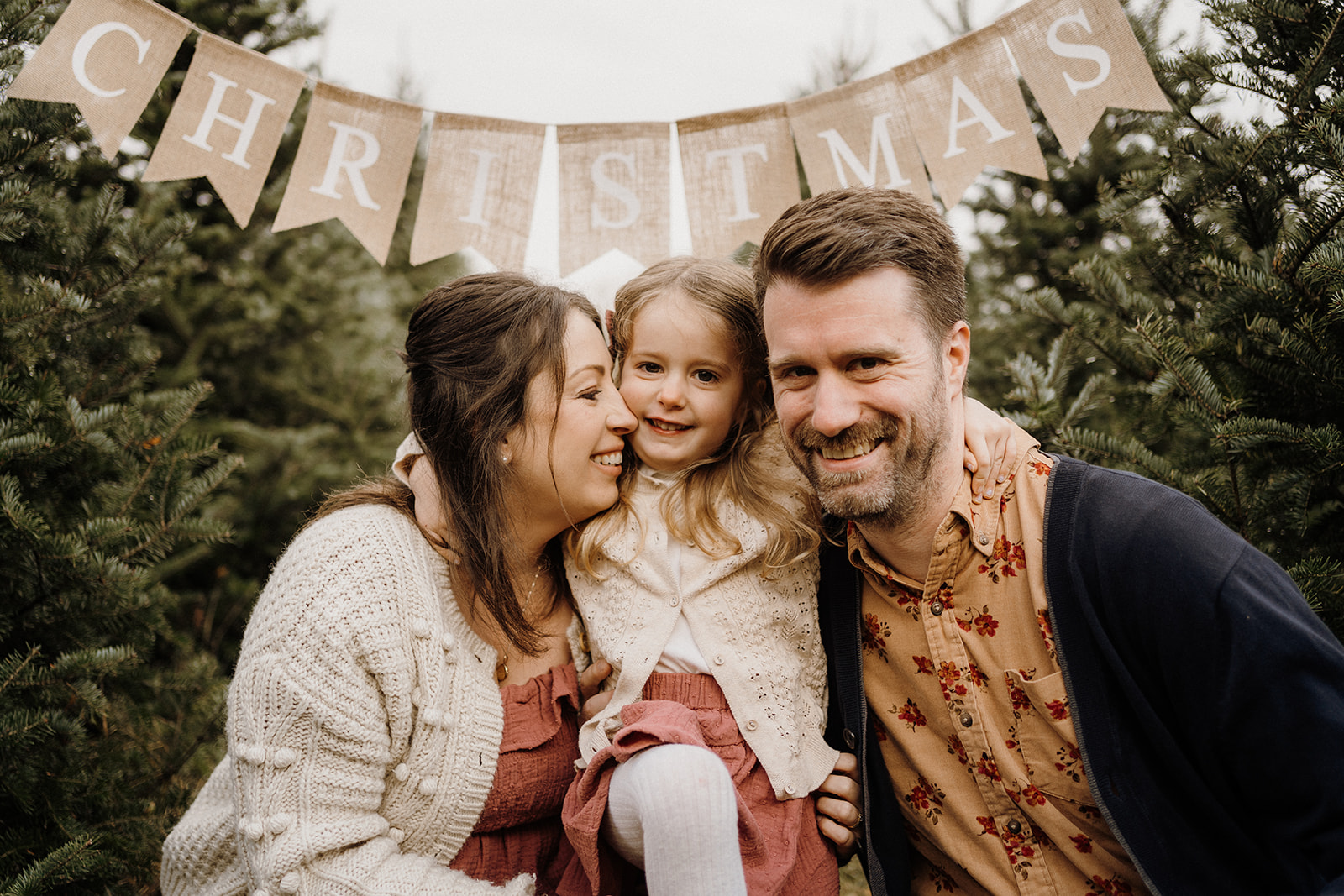 A family of three underneath a 'Merry Christmas' banner.