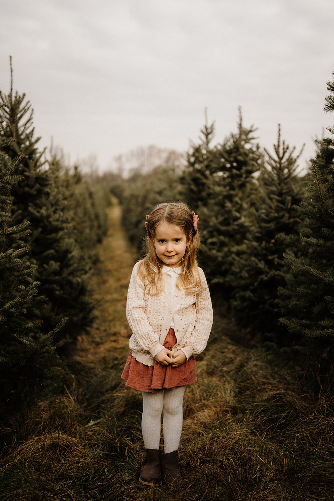 A little girl standing outside between Christmas Trees.