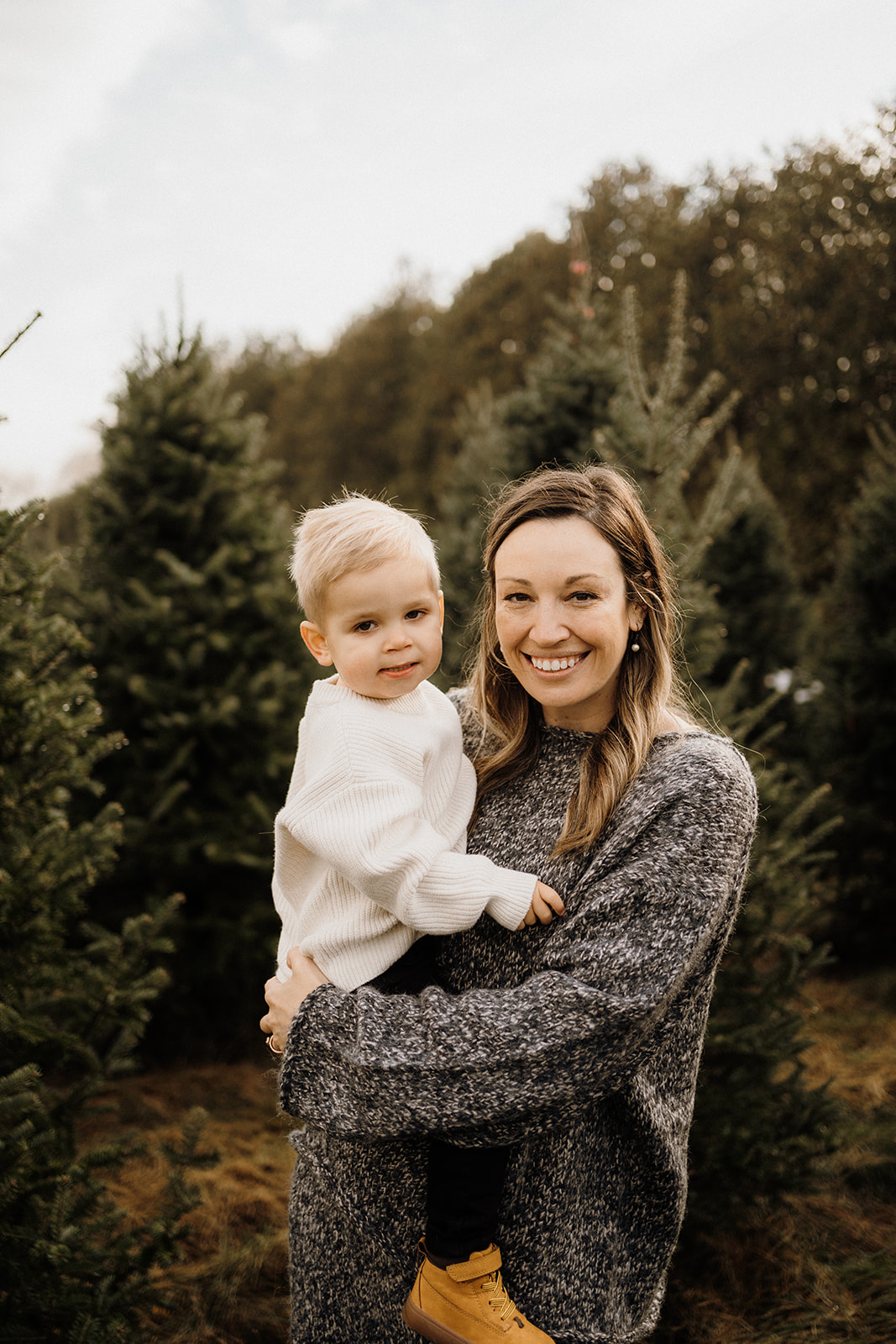 A mother holding her son outside with Christmas Trees in the back.