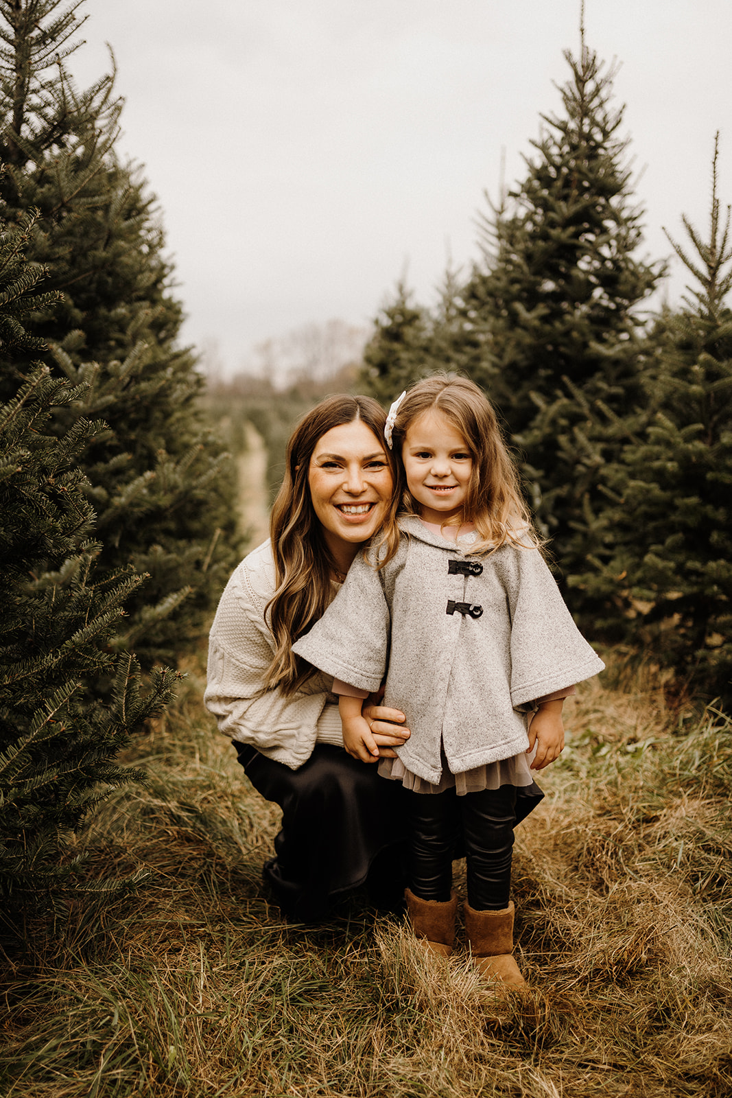 A daughter standing with her mother beside her with Christmas Tress around them.