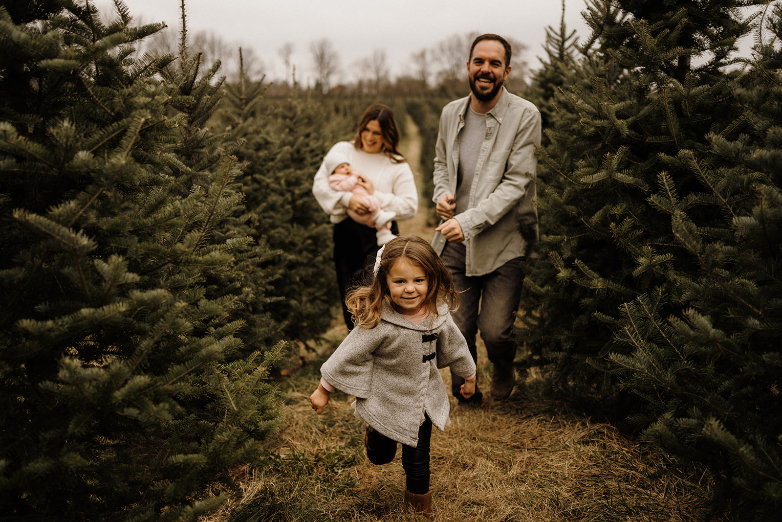 A family of four running between Christmas Trees.