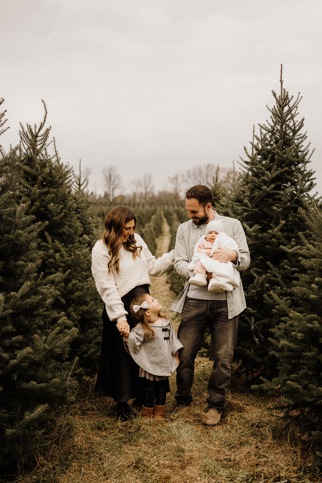 A family of four standing between Christmas Trees.