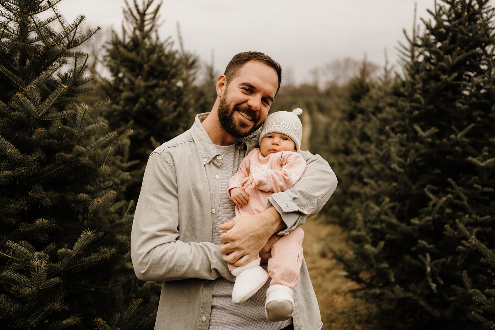 A father holding his child in his arms between Christmas Trees.