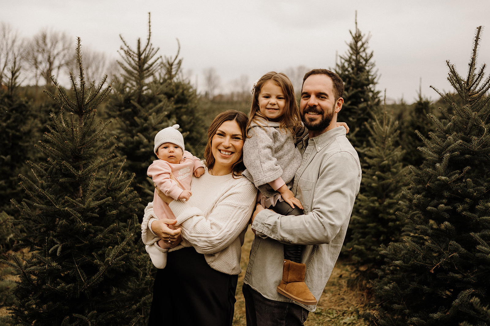 Parents holding their children in their arms outside between Christmas Trees.